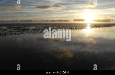 Helle weiße Sonneneinstellung unter grauen Stratocumulus Wolken reflektiert in einem Meer-Wasser-Kanal auf Ebbe Sand Strand, Fairhaven, UK Stockfoto