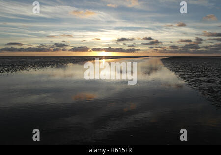 Gelbe Sonneneinstellung unter grauen Stratocumulus Wolken reflektiert in einem Wasserkanal überqueren eine weite Sandstrand, Fairhaven, UK Stockfoto