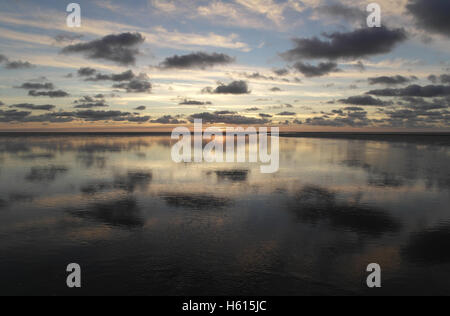 Graue Stratocumulus Wolken reflektiert in einem Meer-Wasser-Kanal auf einer Fläche von Sandstrand, eine gelbe Sonnenuntergang, Fairhaven, UK Stockfoto