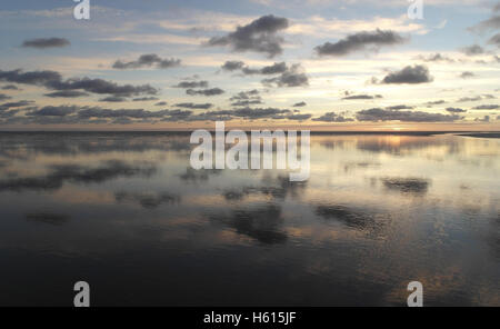 Graue Stratocumulus Wolken reflektiert in weite Meer Kanal Kreuzung Sandstrand Wasserfläche zu gelben sunset Glow, Fairhaven, UK Stockfoto