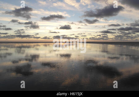 Graue Stratocumulus Wolken reflektiert in einem Meer-Wasser-Kanal überqueren eine weite Sandstrand, eine gelbe Sonnenuntergang, Fairhaven, UK Stockfoto