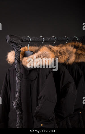 Viele schwarze Mäntel, Jacke mit Fell Kapuze Kleiderständer hängen. Stockfoto