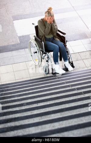 Frau im Rollstuhl vor Treppen im Freien auf der verzweifelten Suche Stockfoto