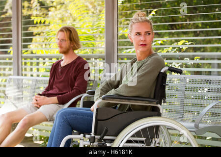 Frau im Rollstuhl im Freien neben jungen Mann auf Bank sitzend Stockfoto