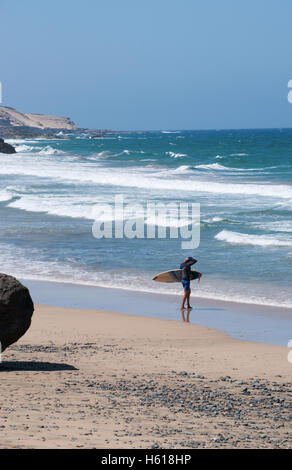 Fuerteventura, Kanarische Inseln, Nordafrika, Spanien: Wellen und ein Surfer, ein Surfbrett an der Playa de Garcey, einem schwarzen Strand an der Westküste Stockfoto