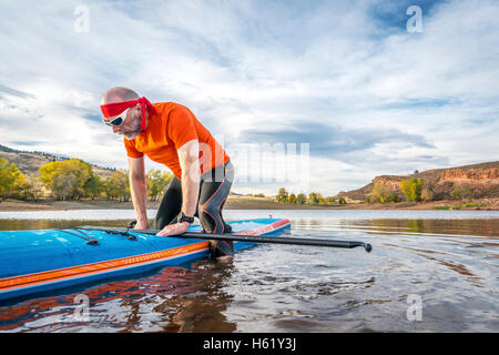 Ein senior Männchen beginnt eine Training auf Stand up Paddleboard an einem ruhigen Bergsee Stockfoto