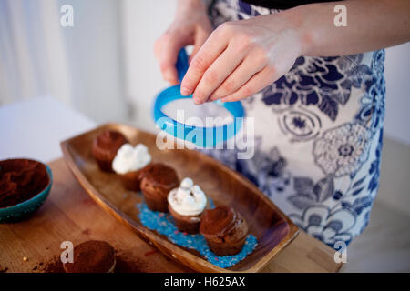 Mädchen dekoriert Cupcakes, Platte, Muffins und Teller mit Zutaten für die Dekoration auf dem Tisch zu halten Stockfoto