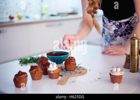 Mädchen zündet die Kerze, schmückt Silvester Feier Muffins, Schokolade Muffins auf Tisch Stockfoto