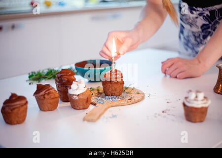 Mädchen zündet die Kerze, schmückt Silvester Feier Muffins, Schokolade Muffins auf Tisch Stockfoto