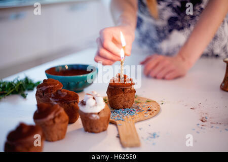 Mädchen zündet die Kerze, schmückt Silvester Feier Muffins, Schokolade Muffins auf Tisch Stockfoto