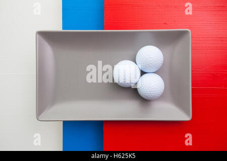 Graue Keramik Teller mit Golf-Ausrüstungen auf über weißen, blauen und roten Holztisch, Rechteck Schale Stockfoto