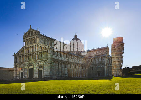 Kathedrale von Pisa mit Glockenturm, die gegen die aufgehende Sonne geneigt ist. Italienische Wahrzeichen auf dem grünen Rasen der Kathedrale Bogen Stockfoto