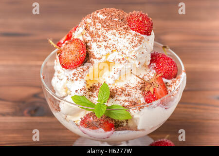 köstliches Dessert rosa Eisportionierer mit frischen Erdbeeren, bestreut Schokoladenstückchen und Minze in Schüssel auf hölzernen Hintergrund, Stockfoto