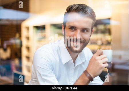 Lächelnd Geschäftsmann Holding Tasse Kaffee hinter Fensterscheibe in einem café Stockfoto