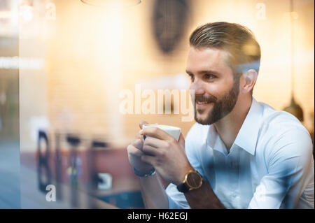 Lächelnd Geschäftsmann Holding Tasse Kaffee hinter Fensterscheibe in einem café Stockfoto