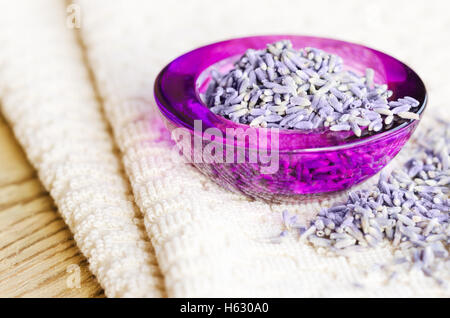 Getrocknete Lavendelblüten in einem lila Glas auf Stoff und Holz. Lavandula Angustifolia mit blassen lila Blüten. Stockfoto