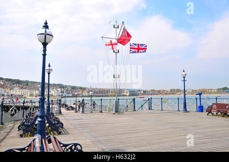 St Geoge Cross, der Handelsmarine Fähnrich und Union Jack-Flaggen auf Swanage Pier, Dorset. Stockfoto