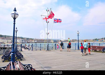 St Geoge Cross, der Handelsmarine Fähnrich und Union Jack-Flaggen auf Swanage Pier, Dorset. Stockfoto