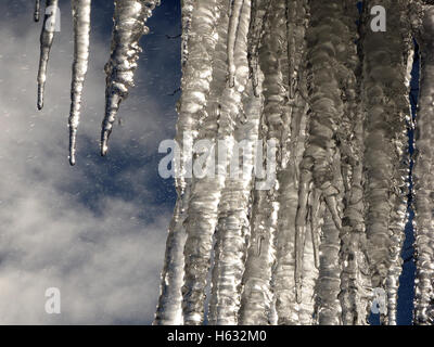 dramatische gefrorenen Vorhang aus hellen Spitzen Eiszapfen hängen gegen blauen Himmel mit weißen Wolken und eisigen Tröpfchen Stockfoto