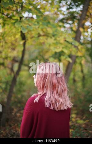 Ein Teenager-Mädchen mit rosa Haaren wie aus einem Winkel, im Freien in einem Waldgebiet. Stockfoto