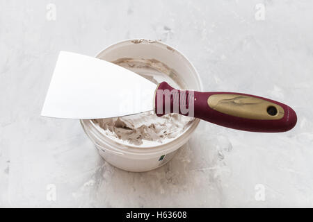 Spachtel aus Metall mit Kunststoffgriff am Rohr mit Putty auf dem Betonboden Stockfoto