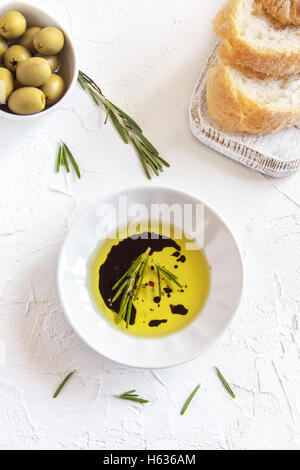 Bio-Olivenöl mit Rosmarin, Balsamico-Essig und Gewürzen über weißen Stein Hintergrund mit Textfreiraum, gesunde Ernährung Konzept