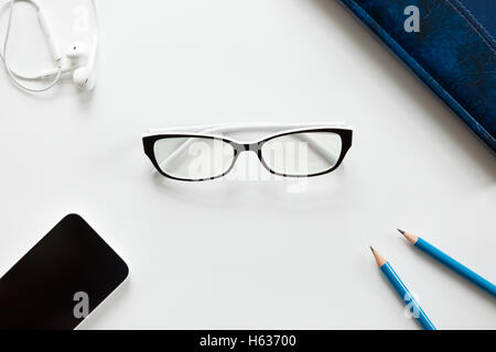 Weißer Schreibtisch mit Brille, Stifte, Ohrhörer und mobile Stockfoto