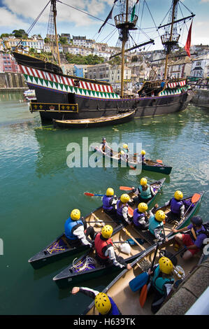 Junge Leute an der Summer School in Brixham Lernen ein Kanu im Hafen mit der Hälfte Nachbau des Golden Hind zu verwenden Stockfoto