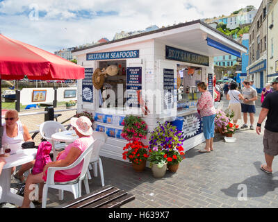 Frau kaufen Meeresfrüchte Sandwiches an sauber und bunt Meeresfrüchte Kiosk in Brixham Harbourside an einem sonnigen Sommer Stockfoto