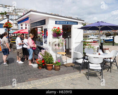 Frau kaufen Meeresfrüchte Sandwiches an sauber und bunt Meeresfrüchte Kiosk in Brixham Harbourside an einem sonnigen Sommer Stockfoto