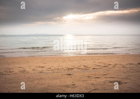 Ruhigen Meer bei Sonnenuntergang Strand in sanften Tönen mit Sonnenlicht durch die Wolken Stockfoto