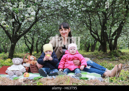 Mutter mit Zwillingen auf Plaid im Freien im Apfelgarten Stockfoto