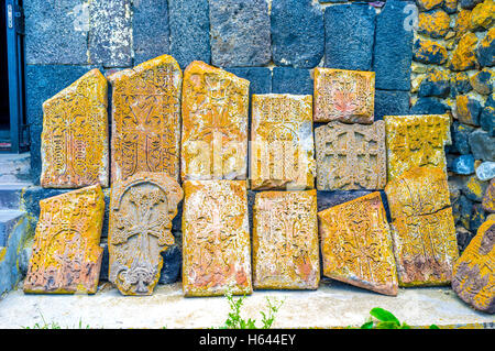 Die gebrochenen mittelalterlichen Khachkars, bedeckt mit Moos und Flechten neben schwarzen Kirchenmauer des Sevanavank Klosters, Sevan, Armenien Stockfoto