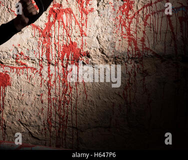 Blut befleckte Wand- und männliche Hand, die eine Säge in einem Halloween-Horror-Konzept Stockfoto