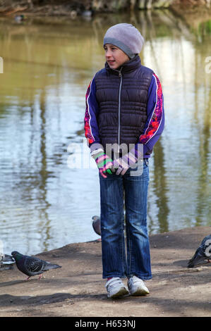 ein Teenager-Mädchen stehen Betwin Tauben Vögel am Ufer eines Teiches Stockfoto