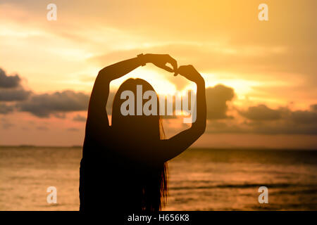 Frau Hände bilden ein Herz mit Sonnenuntergang silhouette Stockfoto