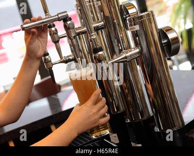 Eine Dame ergießt sich einen Pint Bier in einem Pub aus neue Chrom Armaturen an der Bar in einem Longdrinkglas gerade. Stockfoto