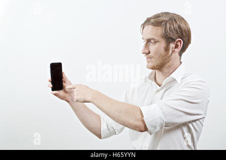 Jungen Erwachsenen Mann im weißen Hemd hält ein Telefon und Punkten Sie mit dem Finger Stockfoto