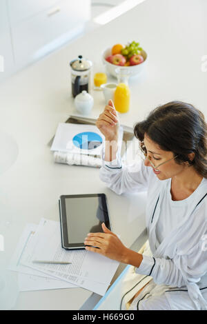 Frau im Bademantel arbeiten bei digital-Tablette am Küchentisch Stockfoto