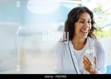 Lachende Frau im Bademantel Trinkwasser Stockfoto