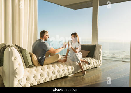 Paar, toasten Weingläser auf luxuriösen getufteten Chaiselongue mit Blick aufs Meer Stockfoto