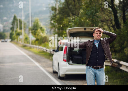 Trampen - Laufwerke. Junger Mann mit erhobener Hand vor Auto unterwegs Stockfoto