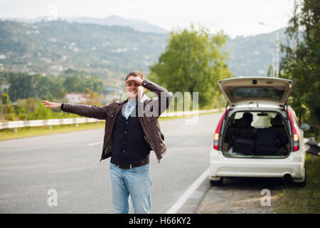 Trampen - Laufwerke. Junger Mann mit erhobener Hand vor Auto unterwegs Stockfoto