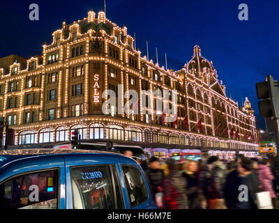 Kaufhaus Harrods im Winter mit Einkäufern verwischen nachts die geschäftige Gegend von ULEZ mit dem Season Sale-Schild Käufer und vorbeifahrende Taxis Knightsbridge London SW1 Stockfoto