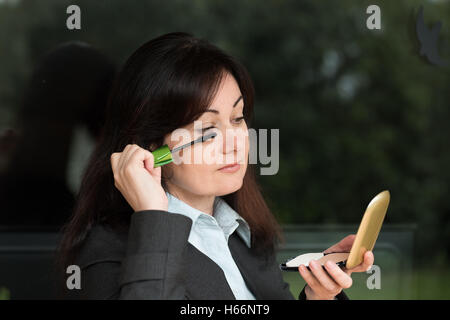 Frau mittleren Alters in Business-Anzug setzt ihre Augen make-up Stockfoto