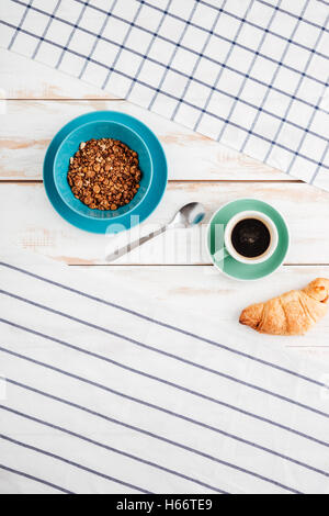 Hafer-Müsli, Kaffee, Croissant mit gestreiften und karierten Servietten auf hölzernen Hintergrund Stockfoto