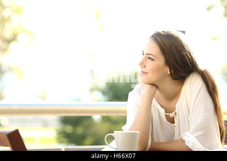 Nachdenkliche Frau denken und Blick auf Seite sitzen in einer Bar oder einem Haus Terrasse Stockfoto