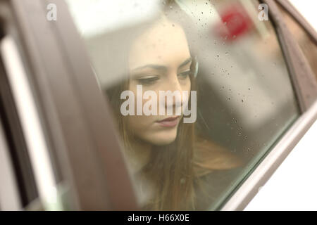 Closeup Portrait besorgt Auto Passagier Blick auf Seite durch das Fenster in einem traurigen Regentag Stockfoto