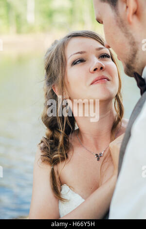 Braut und Bräutigam stehen Arm in Arm gegen den Hintergrund Gras- und Seen. Stockfoto