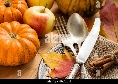 Thanksgiving-Tischdekoration: Geschirr, Teller, Kürbisse, Äpfel, Laub auf Tisch. Nahaufnahme Stockfoto